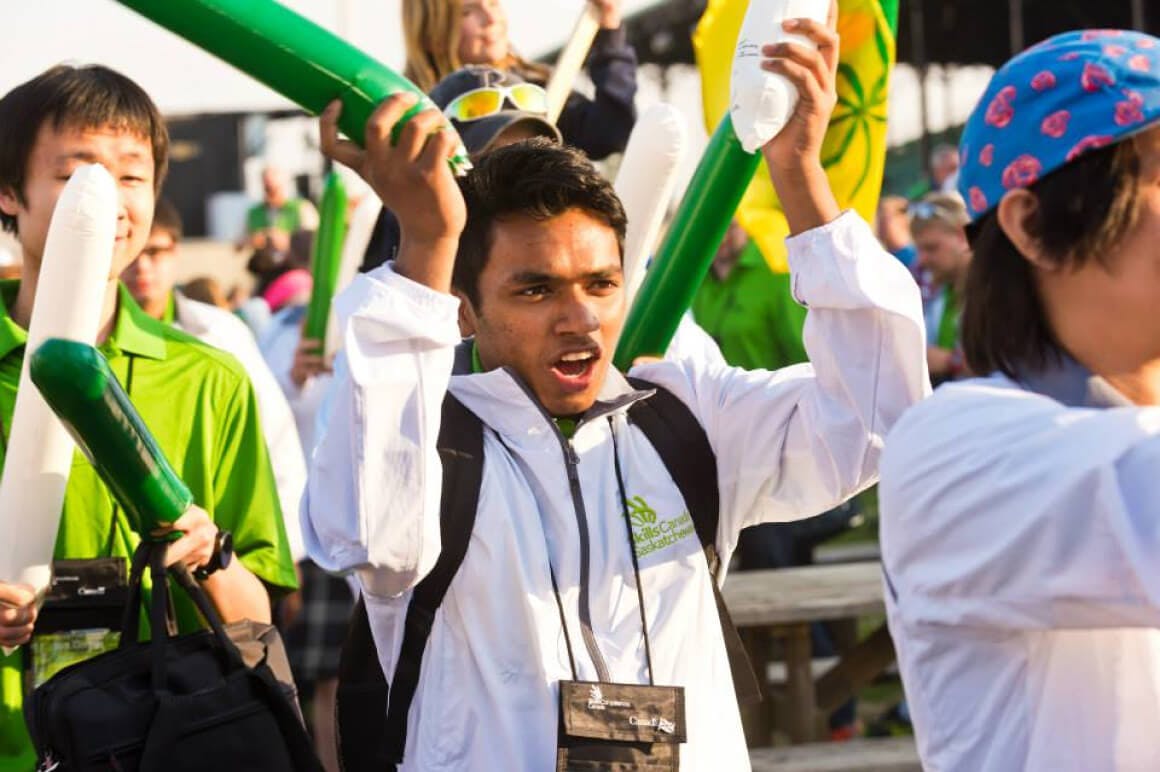 Event photo of students and teachers representing the province of Saskatchewan showing their team spirit by holding up inflatable cheering sticks. They are seen marching towards the main stage during the opening ceremony.